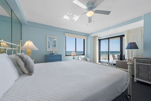 A hotel room with a large bed, a ceiling fan, a window with a view, a desk, and a chair.