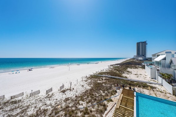A beach view with a swimming pool, a tall building, and a sandy beach.