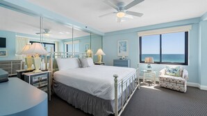A bedroom with a bed, bedside tables, a chair, a ceiling fan, a large window with a view, and a mirror. - Broadmoor 304- Epic Vacations Start Here! Book Now! (Orange Beach)