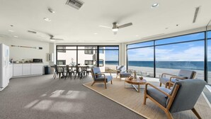 A spacious living area with a large window overlooking the beach, a dining area, and a kitchen with white cabinetry. - Broadmoor 304- Epic Vacations Start Here! Book Now! (Orange Beach)