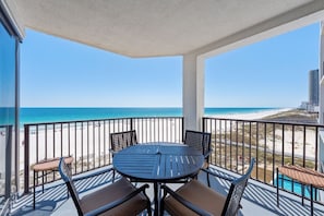 A balcony with a round table and chairs, overlooking a beach and ocean.