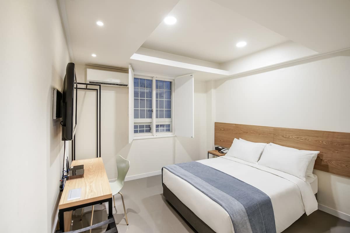 A modern bedroom with a bed, bedside table, chair, and a window.