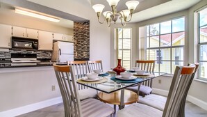 A modern kitchen with built-in appliances, a dining area with a glass table and striped chairs, and large windows providing natural light. - Remodeled 3/2 condo minutes to Parks, shopping and entertainment (Kissimmee)