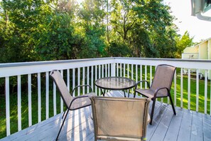 Une terrasse en bois avec une balustrade blanche, deux fauteuils en osier et une petite table ronde.