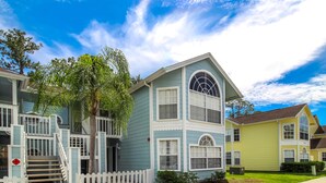 A row of two-story houses with a white picket fence, a palm tree, and a clear blue sky. - Remodeled 3/2 condo minutes to Parks, shopping and entertainment (Kissimmee)