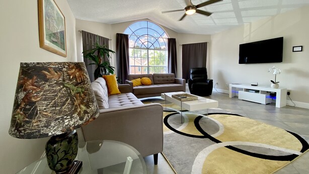 A modern living room with a sofa, coffee table, and a ceiling fan. - Remodeled 3/2 condo minutes to Parks, shopping and entertainment (Kissimmee)