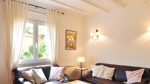 Een woonkamer met een bruine leren bank, een houten salontafel en een raam met gordijnen. Er staat een lamp op een bijzettafeltje en een schilderij hangt aan de muur.
