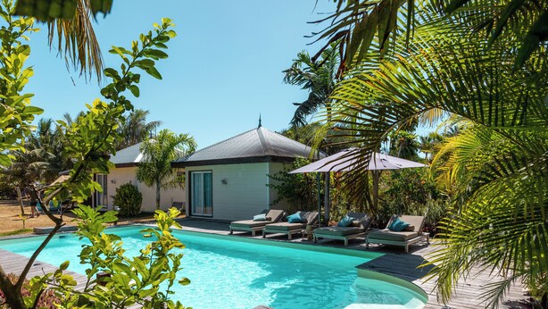 A swimming pool with lounge chairs and a small building in the background. - Poé Côté Lagon Beach Bungalows (Bourail)