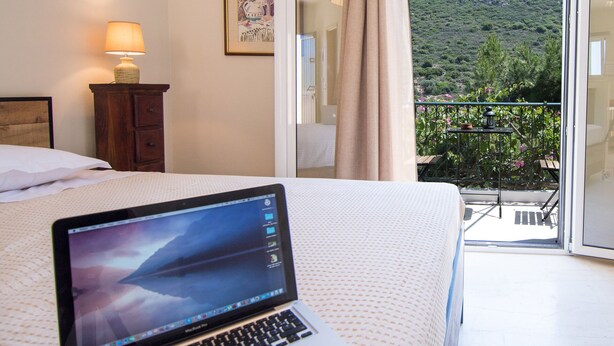 A laptop on a bed in a room with a balcony, a lamp, and a painting on the wall. - CASA BUGANVILLA 5 in Minia (Argostoli)