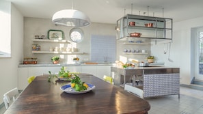 Een moderne keuken met een houten eettafel, een hanglamp en koperen kookgerei op planken.