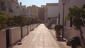 A paved pathway lined with potted plants and buildings on either side. - Delightful family villa in secure gated community with large pool. (Puerto De Mazarrón)