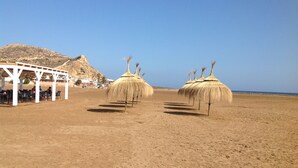 A beach with thatched umbrellas and a covered seating area with tables and chairs. - Delightful family villa in secure gated community with large pool. (Puerto De Mazarrón)