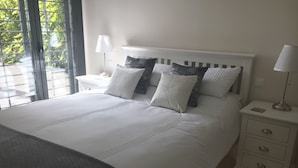 Une chambre avec un grand lit, du linge de lit blanc, deux tables de chevet avec des lampes et une vue sur la verdure par la fenêtre.