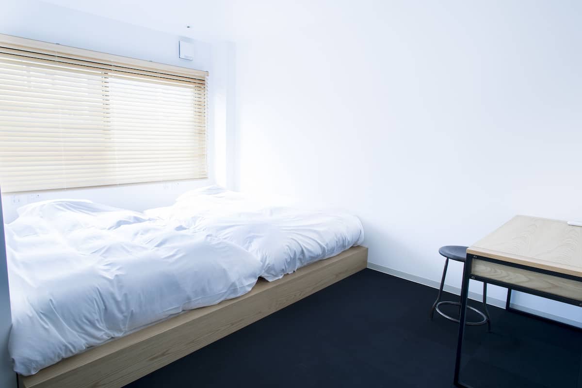 A minimalist bedroom with a bed, a small table, and a window with blinds.