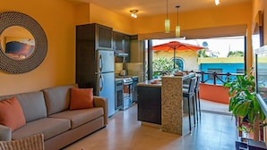 Una cocina moderna con electrodomésticos de acero inoxidable, un comedor con mesa y sillas, y un amplio ventanal con vista a un edificio azul.