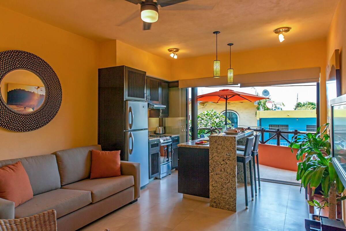 A modern kitchen with stainless steel appliances, a dining area with a table and chairs, and a large window overlooking a blue building.