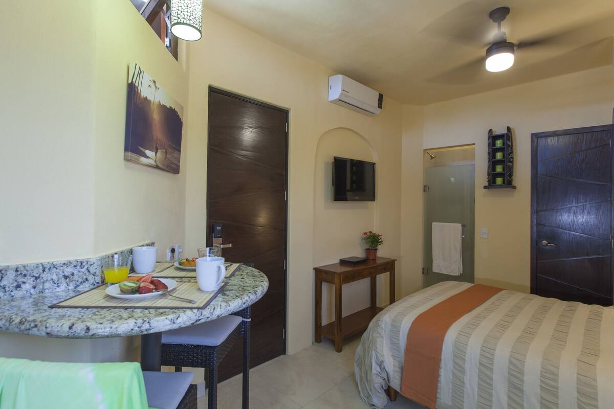A hotel room with a bed, a small table with breakfast items, a TV, and an air conditioning unit.