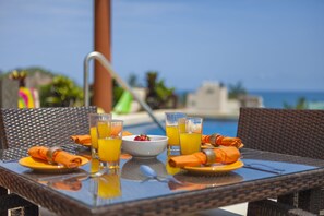 A table set with orange napkins, a bowl of strawberries, and glasses of orange juice, overlooking a pool and the sea. - Beach Break Suites Sayulita (Sayulita)