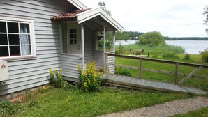 A house with a porch, a wooden deck, and a gravel path leading to a dock by a lake.