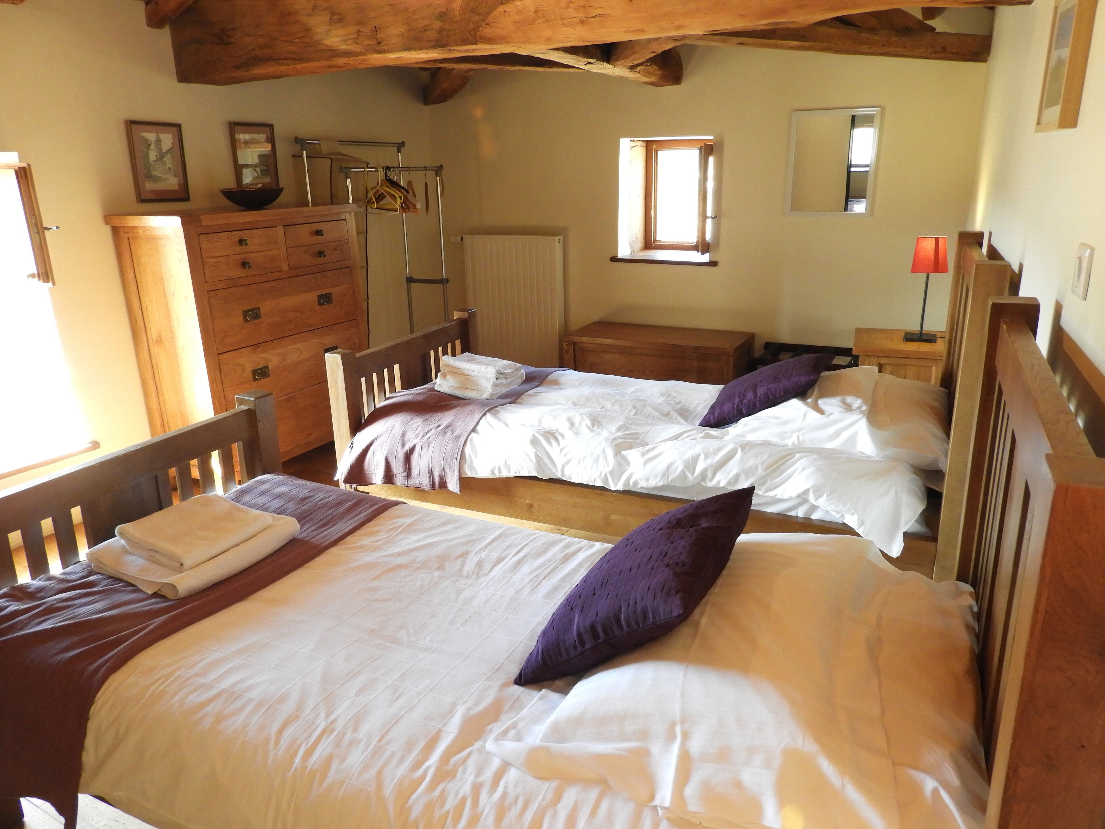 A room with two wooden beds, a wooden dresser, a radiator, and a window with natural light.