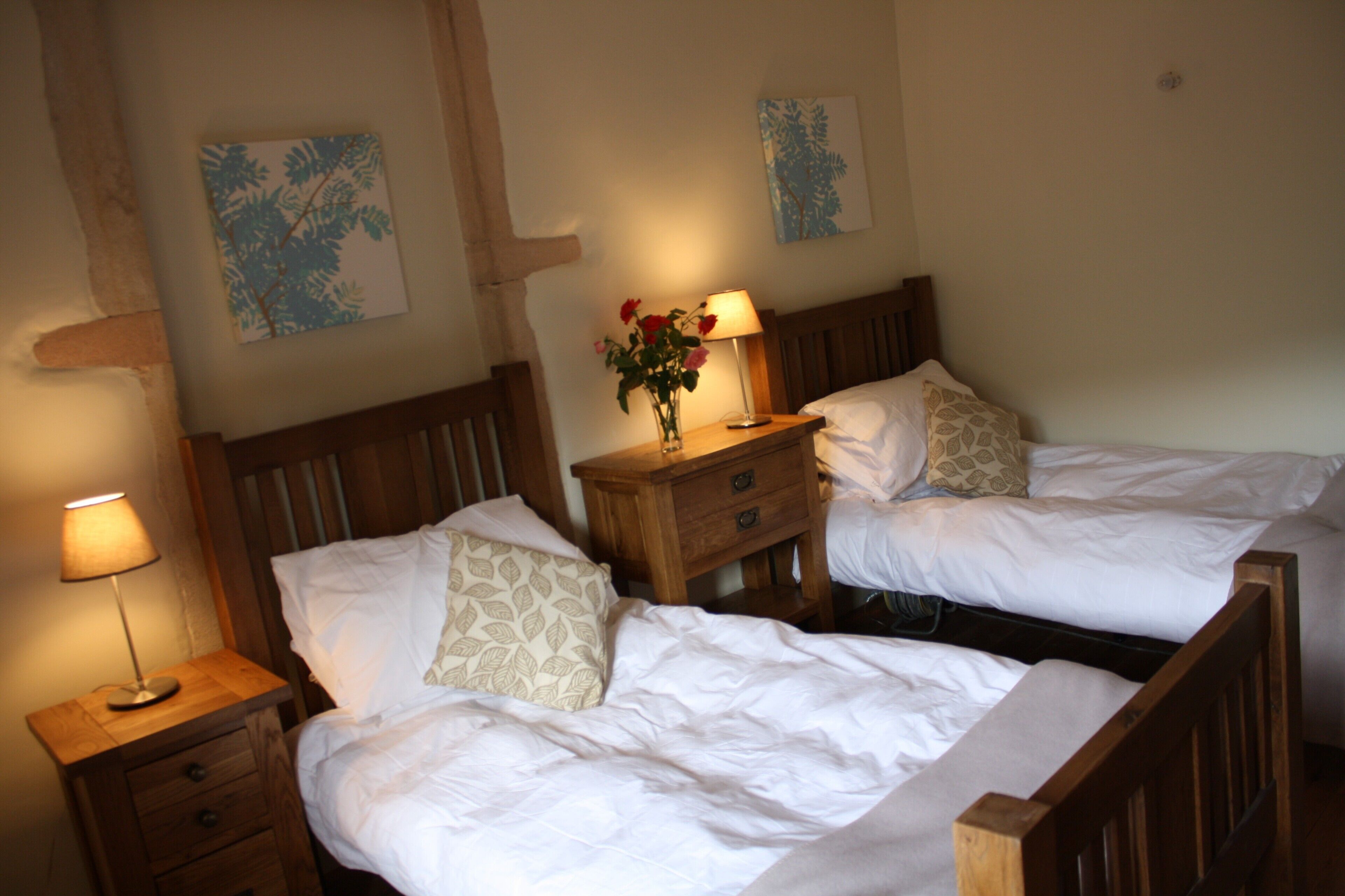 Een slaapkamer met twee bedden, houten hoofdborden, nachtkastjes met lampen en decoratieve muurkunst.