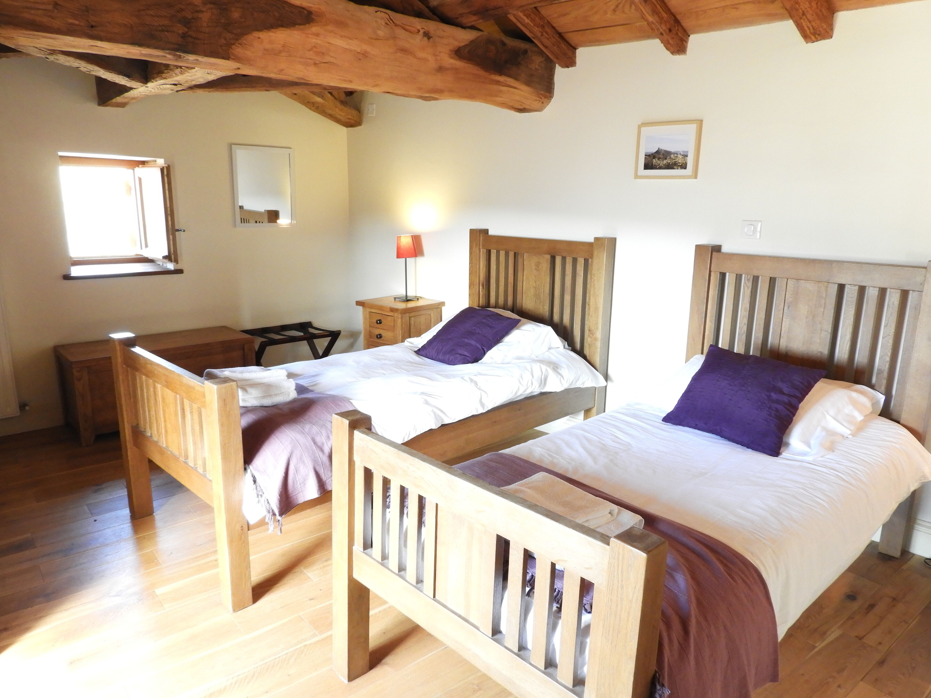 A bedroom with two wooden beds, a desk, a chair, a nightstand with a lamp, and a window.