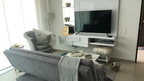 A modern living room with a grey sofa, a TV, and a white console table. - TIVOLI 3 BEDROOM APARTMENT, NEAR BUENAVISTA. (Barranquilla)