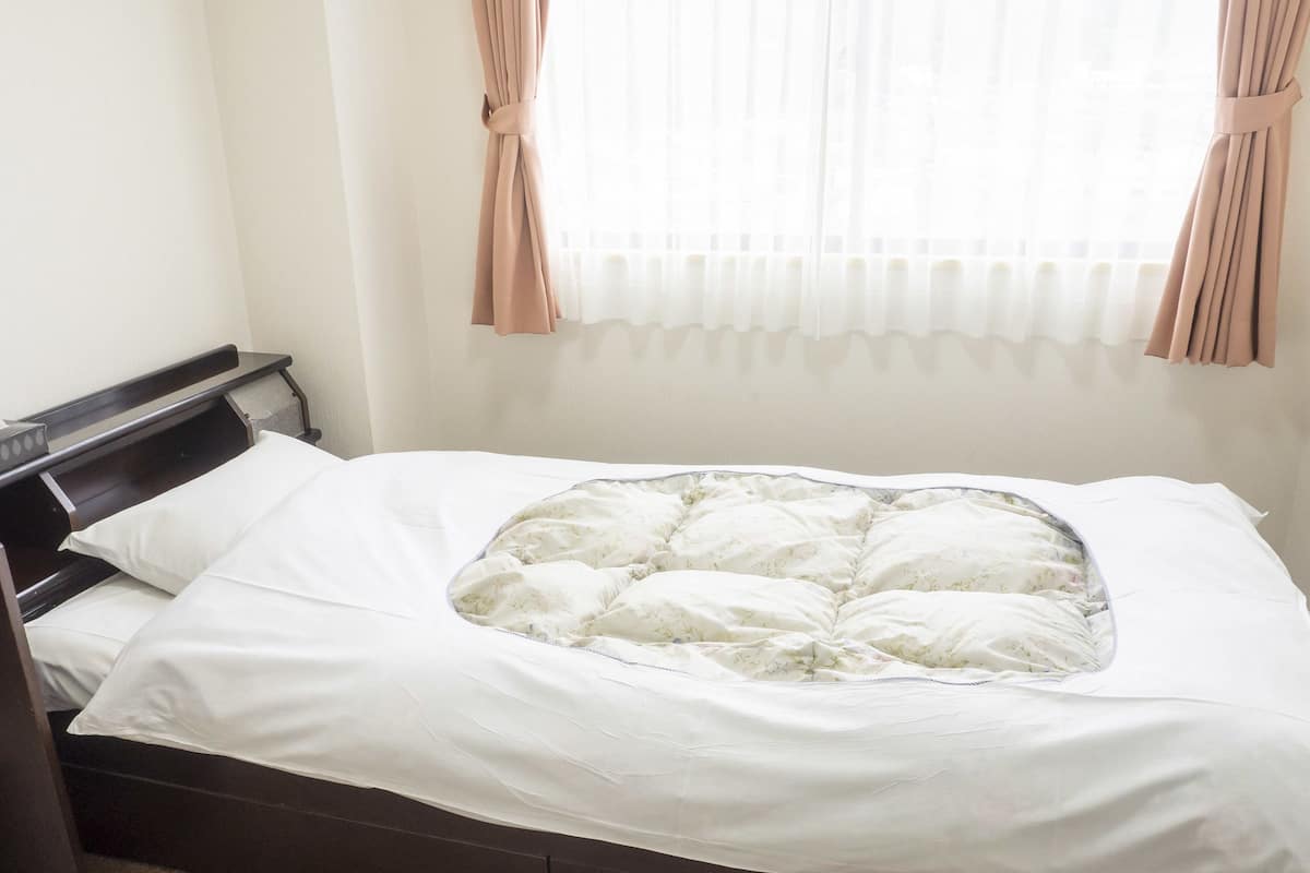 A neatly made bed with a floral-patterned duvet, a wooden headboard, and a window with sheer curtains.