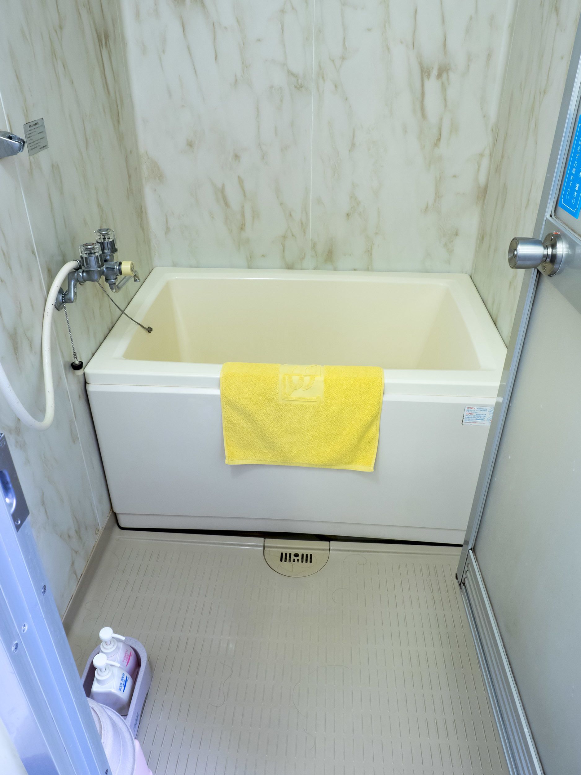 A bathroom with a white bathtub, a yellow towel, and a hand soap dispenser on the floor.