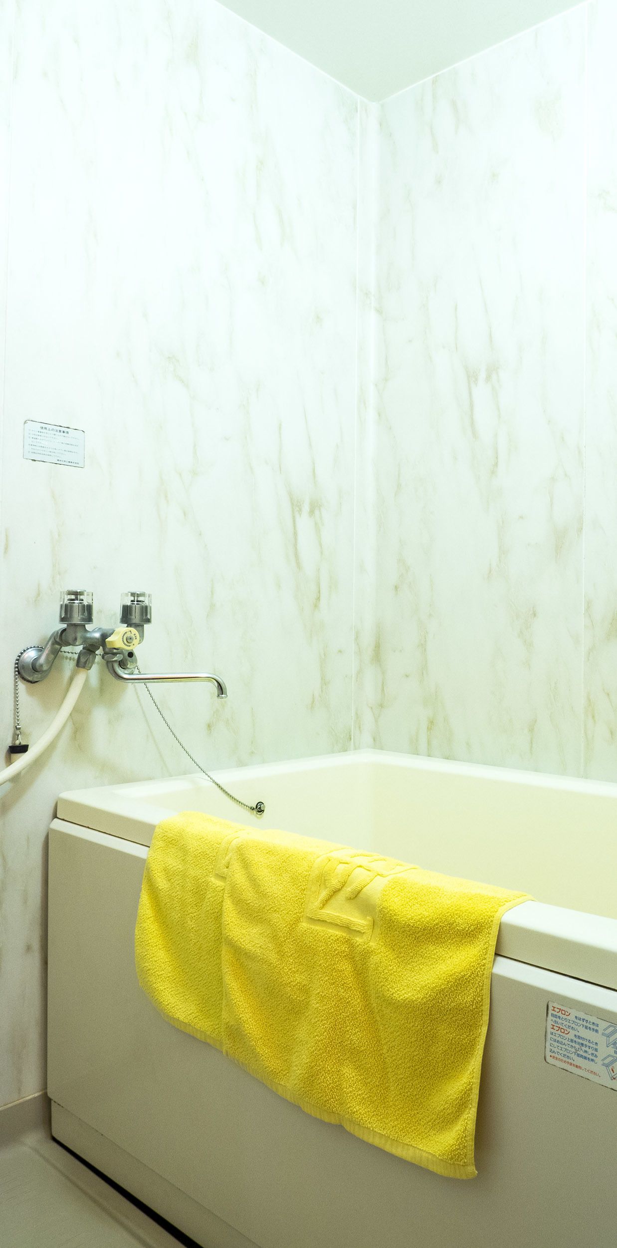 A bathroom with a white bathtub, a yellow towel hanging on the side, and a marble wall.