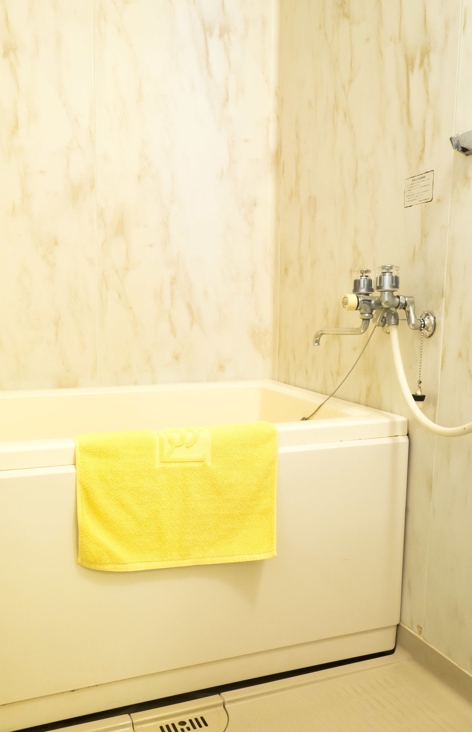 Un baño con bañera, una toalla amarilla y un grifo de ducha.