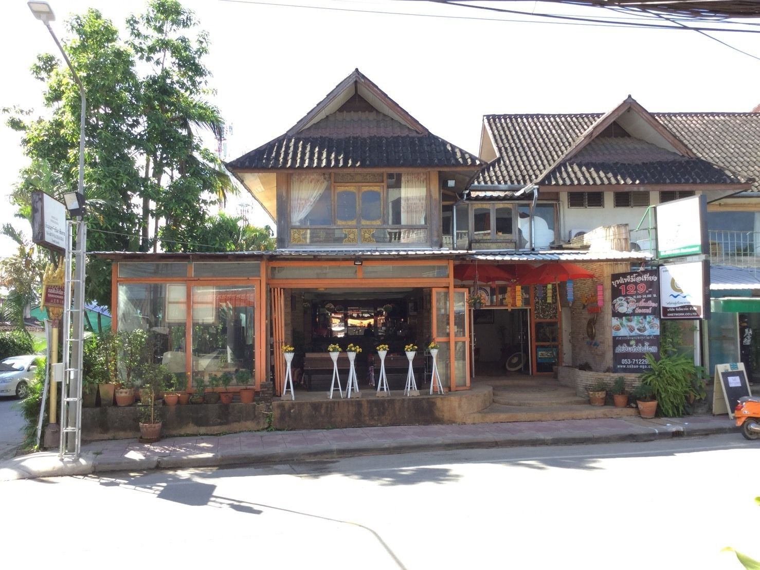 A two-story building with a traditional architectural style, featuring a balcony and a storefront with potted plants.