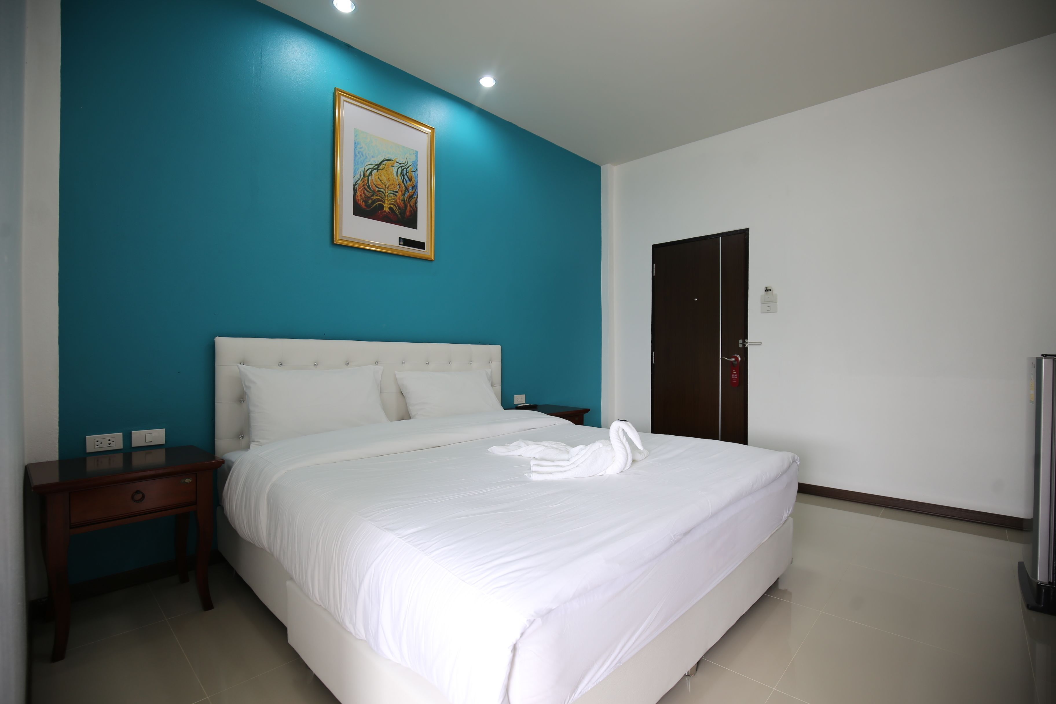 A hotel room with a large bed, a nightstand, a framed picture on the wall, and a door.
