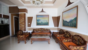 A spacious living area with a high ceiling, ornate wooden furniture, and a large painting of a landscape.