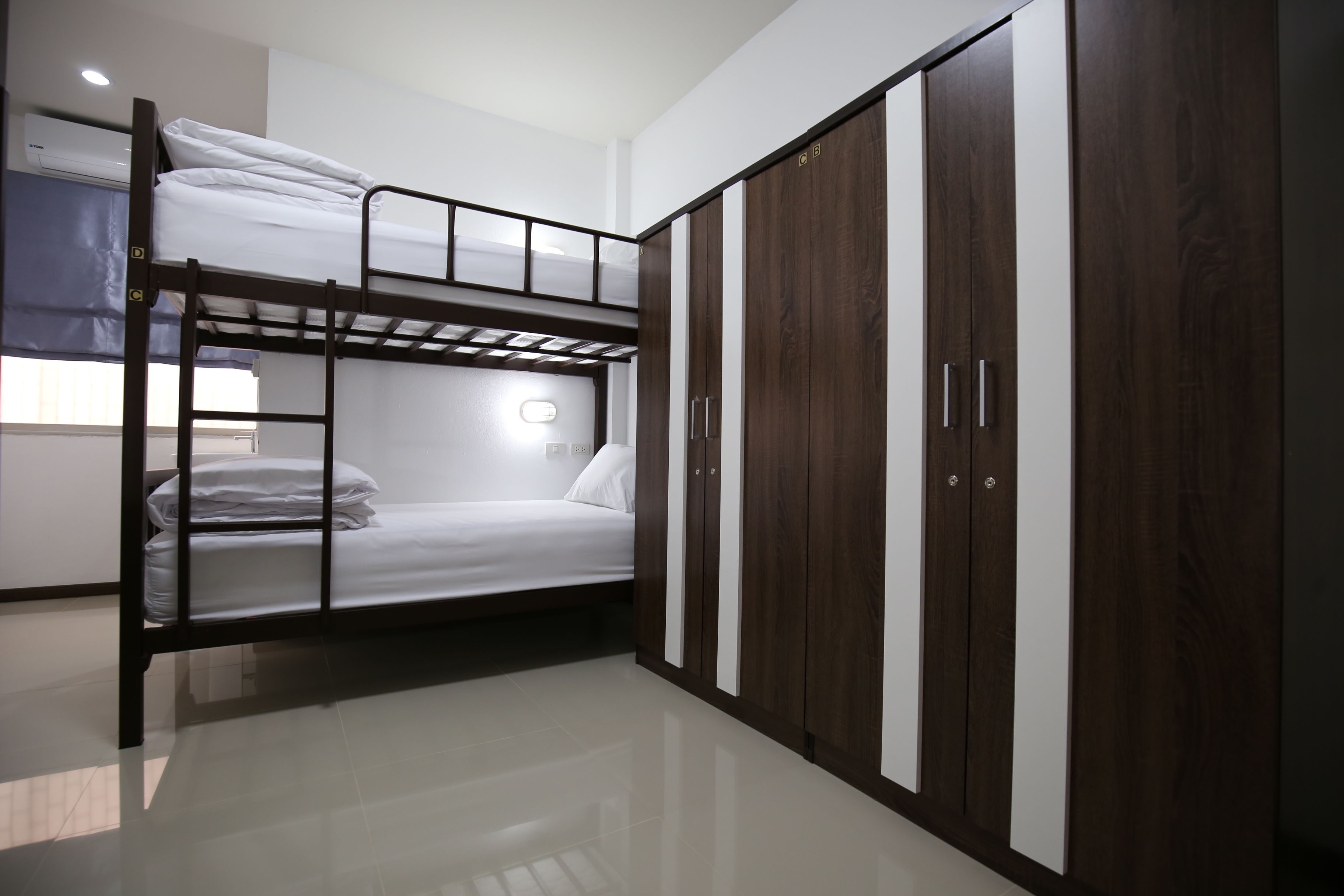 Un lit superposé avec une échelle, une armoire à deux portes et une table de chevet avec une lampe.