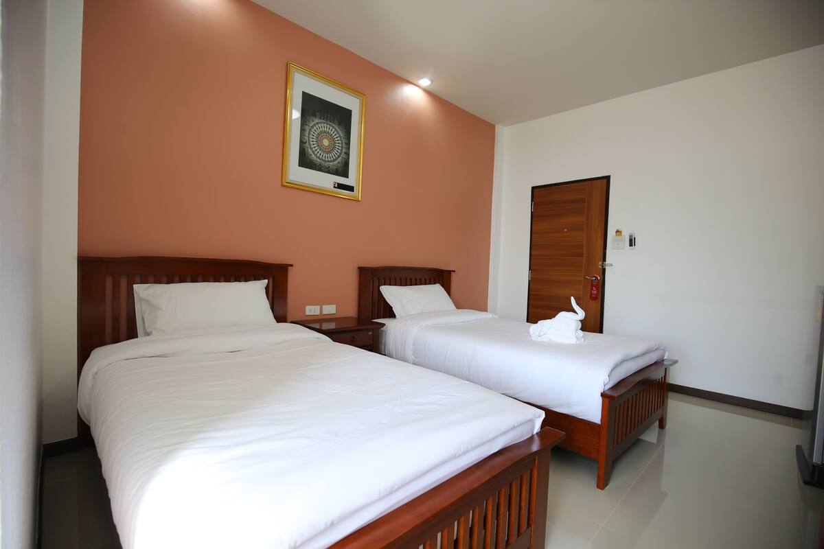 Habitación de hotel con dos camas individuales, cabecera de madera, un cuadro enmarcado en la pared y una puerta con manija.