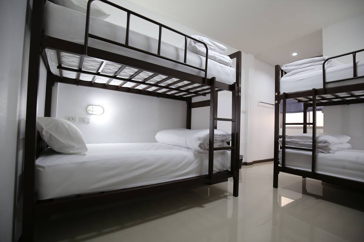 Una habitación con literas, una ventana con cortinas y una lámpara fijada a la pared.