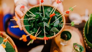 A basket filled with green leafy vegetables, some with colorful edible flowers on toothpicks.