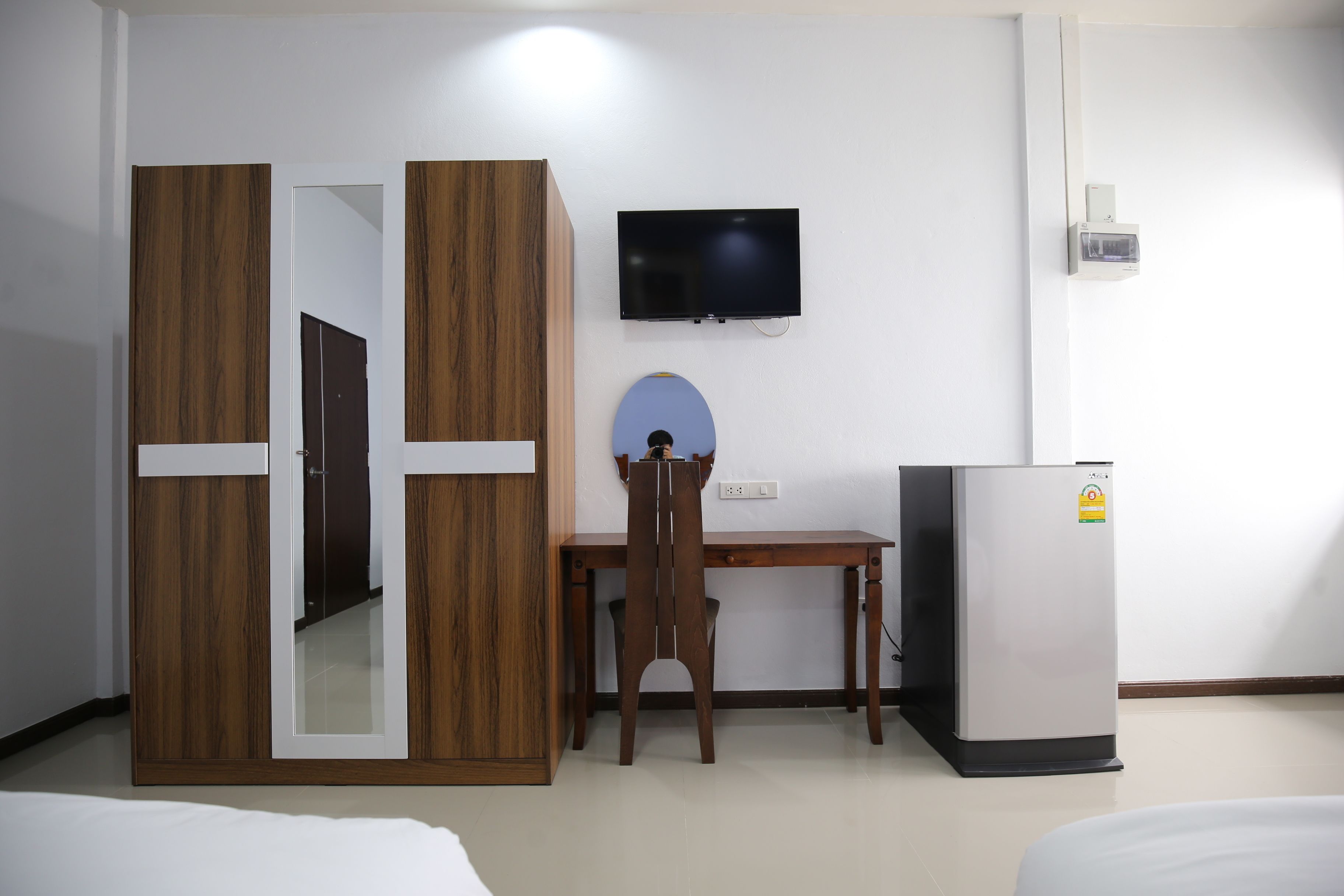 A hotel room with a bed, a wooden wardrobe, a desk with a chair, a television, and a refrigerator.