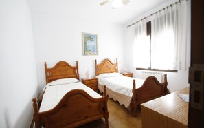 A bedroom with two wooden beds, a nightstand, a table, a ceiling fan, a window with sheer curtains, and a wall-mounted painting. - Villa Lyna by Parc Mont-roig (Miami Playa)