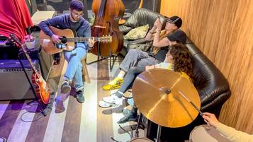 A room with a person playing an acoustic guitar, another person sitting on a couch, and a third person holding a drum.