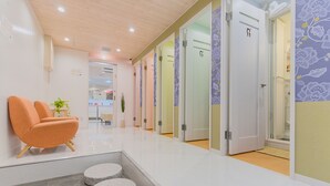 A modern interior with a reception area, a seating area with an orange chair, and a hallway leading to multiple rooms. - Feel Osaka Yu - Hostel (Osaka)