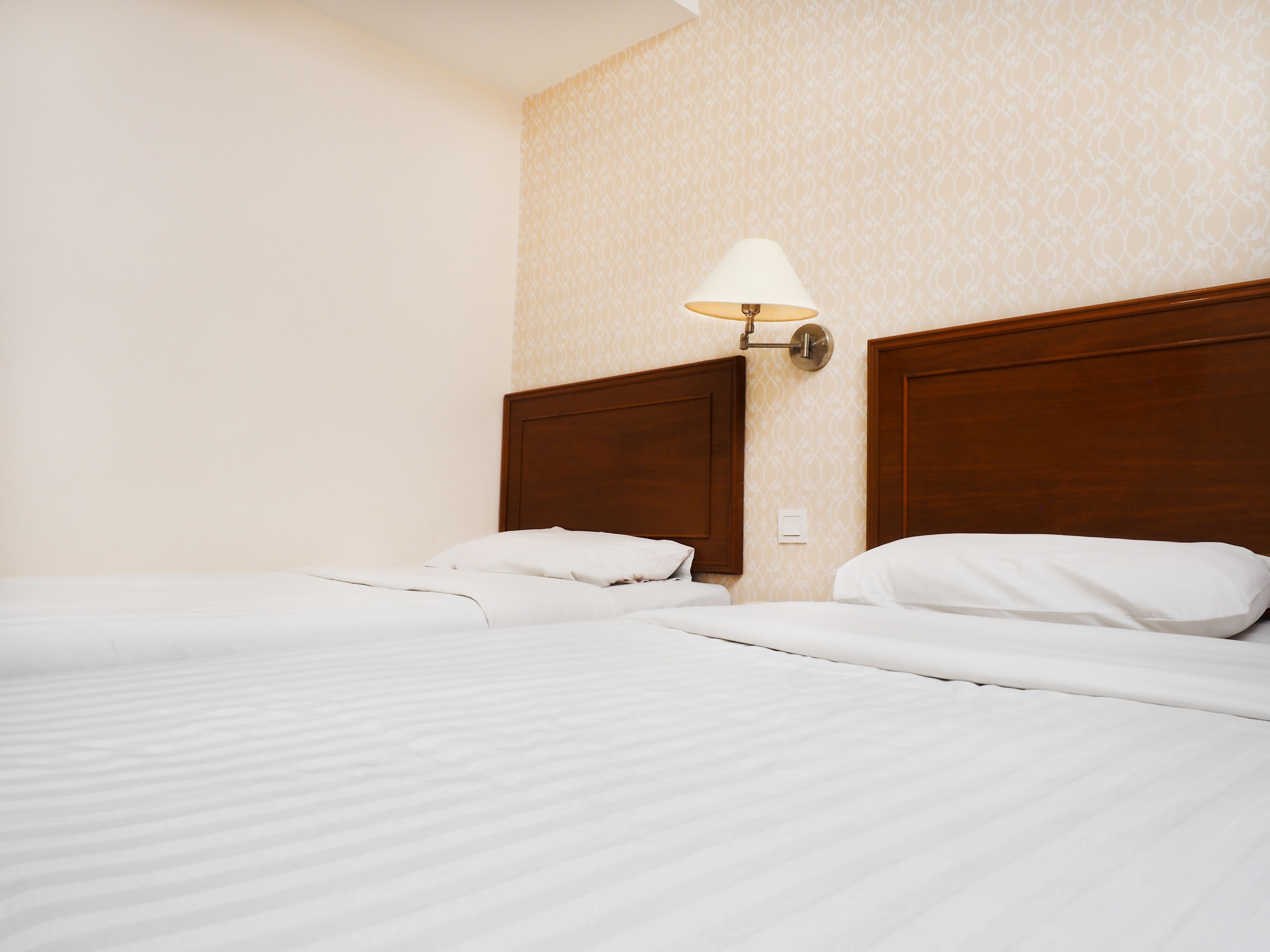 Een hotelkamer met twee bedden, een wandlamp en behang met een patroon.