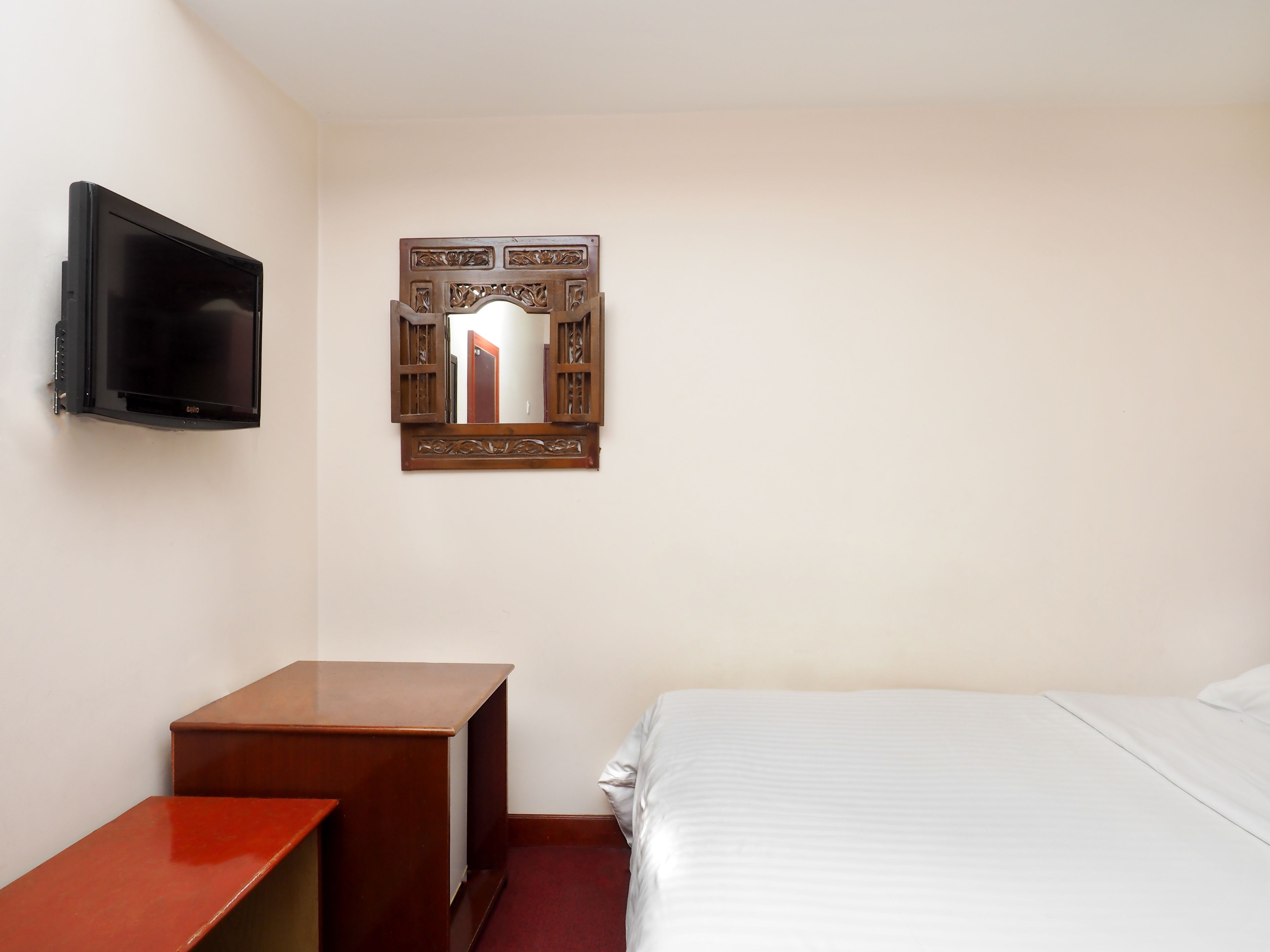 Une chambre d’hôtel avec un lit, une table de chevet en bois, un téléviseur fixé au mur et un miroir doté d’un cadre orné.