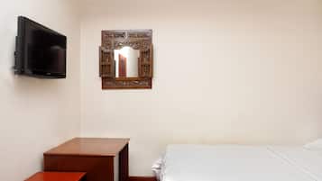 Une chambre d’hôtel avec un lit, une table de chevet en bois, un téléviseur fixé au mur et un miroir doté d’un cadre orné.