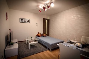 A small, well-lit room with a single bed, a small table with a lamp, a chair, and a TV. - Forest Terrace Tenjin Minami (Fukuoka)
