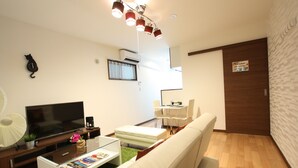 Een moderne woonkamer met een flatscreen-televisie, een witte bank, een glazen salontafel en een eethoek met een witte tafel en stoelen.