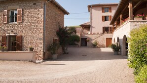 A stone building with a gravel courtyard, wooden shutters, and potted plants. - La Forge - Apartment private terrace, overlooking the pool and Roche de Solutré (Vergisson)