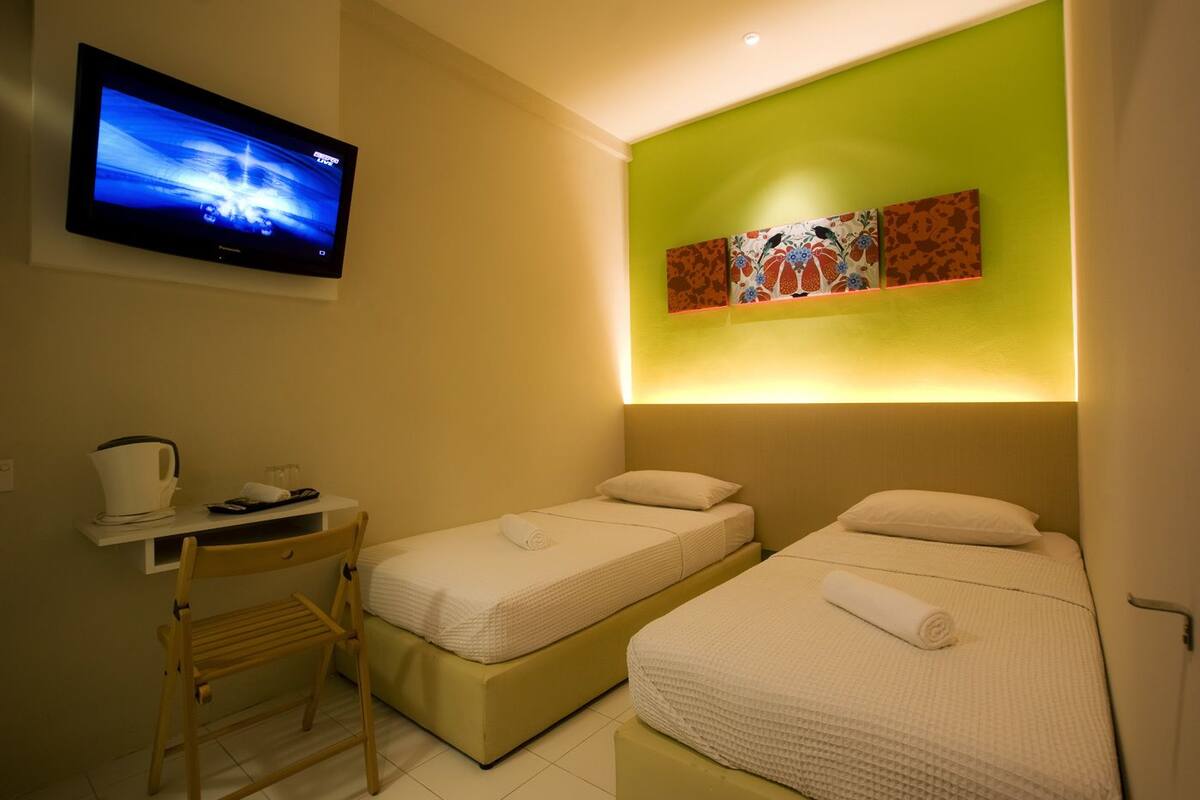 Een hotelkamer met twee bedden, een bureau met stoel, een televisie en een kunstwerk aan de muur.