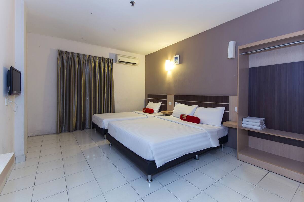 A hotel room with two beds, a TV, an air conditioner, and a wardrobe.